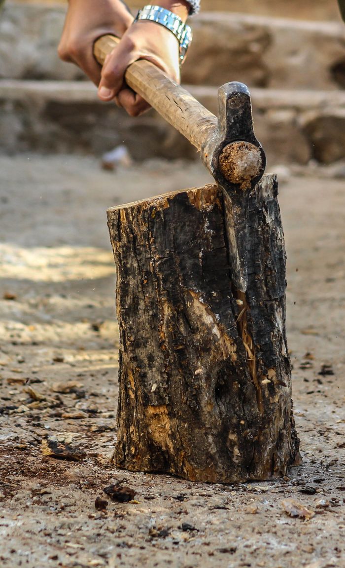 A person chops wood with an axe in an outdoor setting, close-up view.